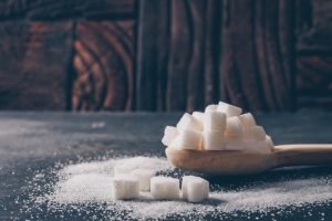 Some white sugar in a spoon on dark background, side view.